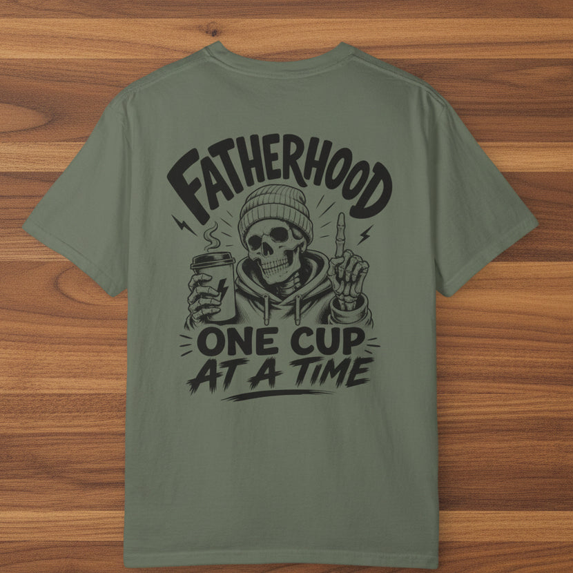 Green Fatherhood Club t-shirt with black Fatherhood One Cup At A Time coffee dad graphic on a woodgrain background.