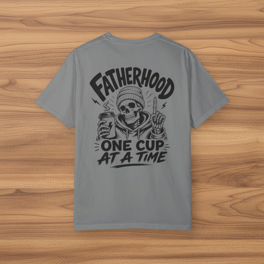 Gray Fatherhood Club shirt with black Fatherhood One Cup At A Time coffee dad graphic on a woodgrain background.