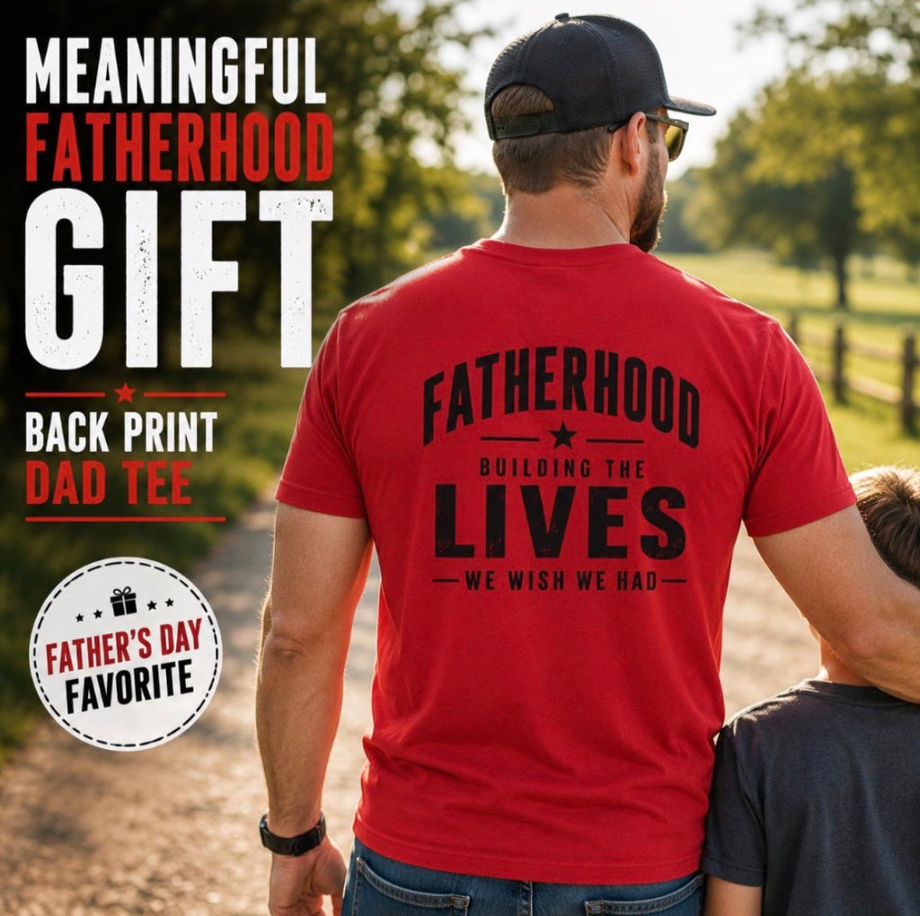 Red Fatherhood graphic T-shirt lifestyle photo worn outdoors, showing the Building the Lives We Wish We Had back print while standing with a child.