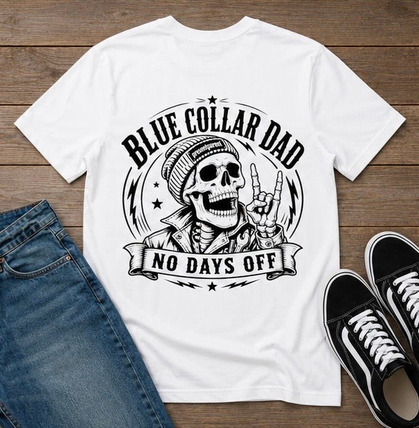 White men’s graphic T-shirt featuring a bold Blue Collar Dad skull illustration with the words “NO DAYS OFF,” displayed on a rustic wood surface beside denim jeans and black sneakers. Hardworking dad shirt for construction workers, mechanics, tradesmen, fathers, husbands, Father’s Day gifts, birthday presents, casual workwear, and everyday blue collar style.