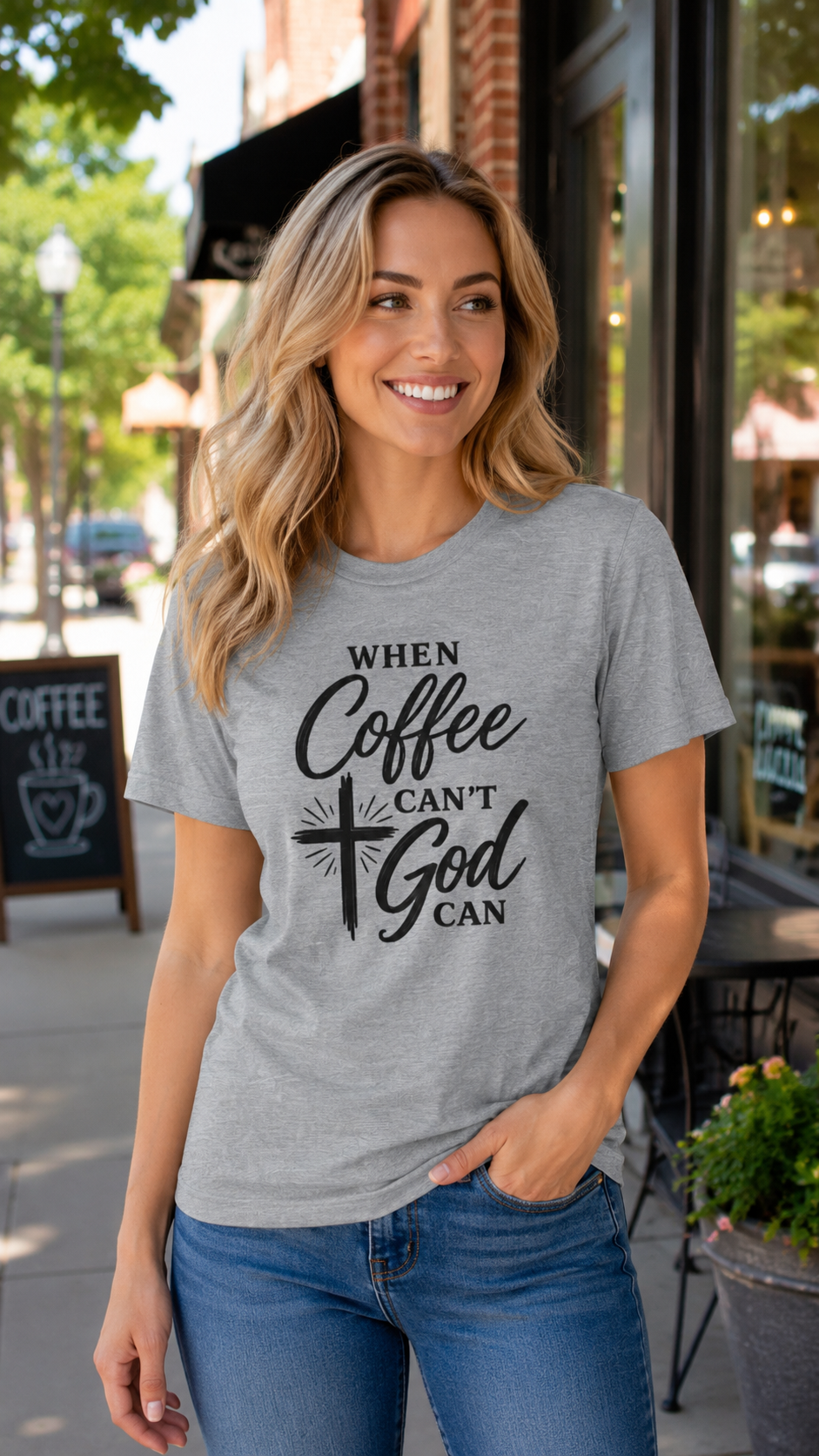 A woman wearing a heather gray graphic t-shirt with the text 'WHEN Coffee CAN'T God CAN' in black script and cross design, standing on a sidewalk in front of a coffee shop.