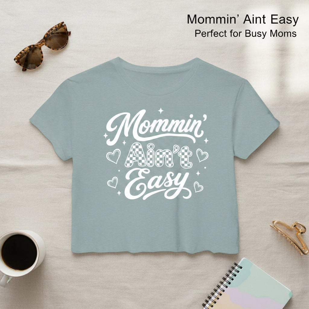 Light blue women’s Mommin Ain’t Easy cropped t-shirt with coffee cup and sunglasses styling props.