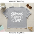 Gray women’s Mommin Ain’t Easy crop top with white mom graphic shown with coffee cup and sunglasses props.