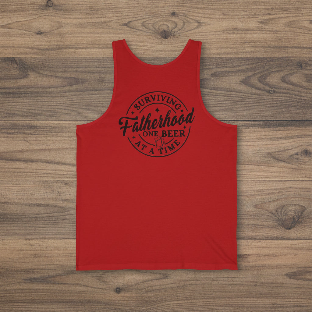 Red Surviving Fatherhood One Beer at a Time tank top with black dad humor text on a woodgrain background.