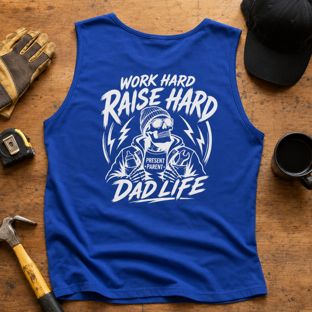 A royal blue sleeveless tank top laid flat on a wooden surface, featuring a large white graphic with the text 'WORK HARD RAISE HARD DAD LIFE' and a skeleton construction worker illustration. Surrounding props include work gloves, a hammer, tape measure, black coffee mug, and a black baseball cap.